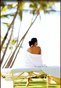 Photo of woman in tropical climate sitting on a massage table looking to sky.